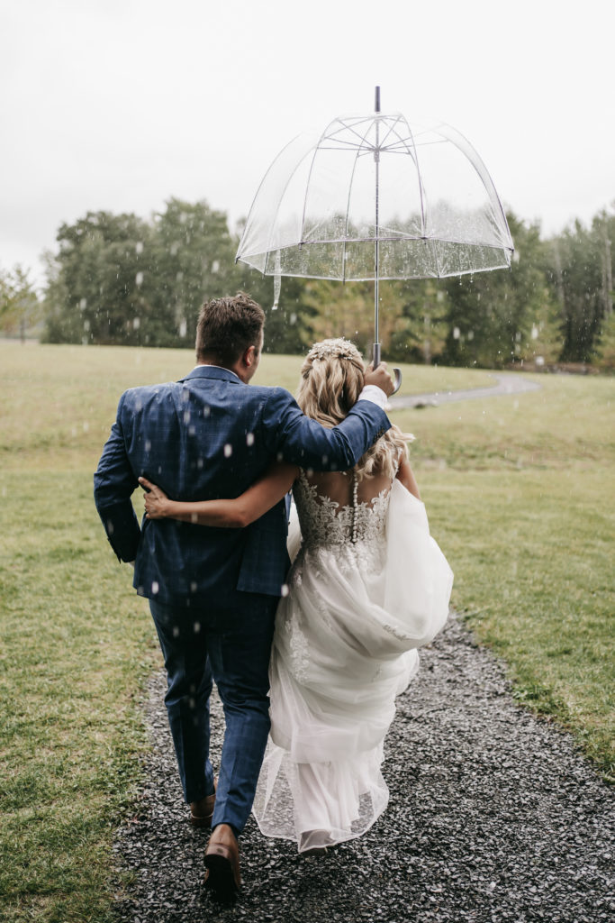 Bride and group take shelter underneath umbrella on their rainy wedding day