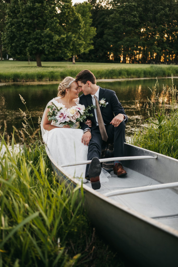Bride and groom sit in a canoe in a pond on their wedding day