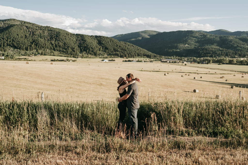 A couple kissing in tall grass surrounded by mountains in Montana.