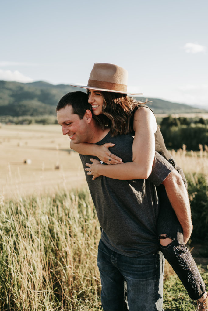 A man giving his fiance a piggyback ride surrounded my mountains in Montana.