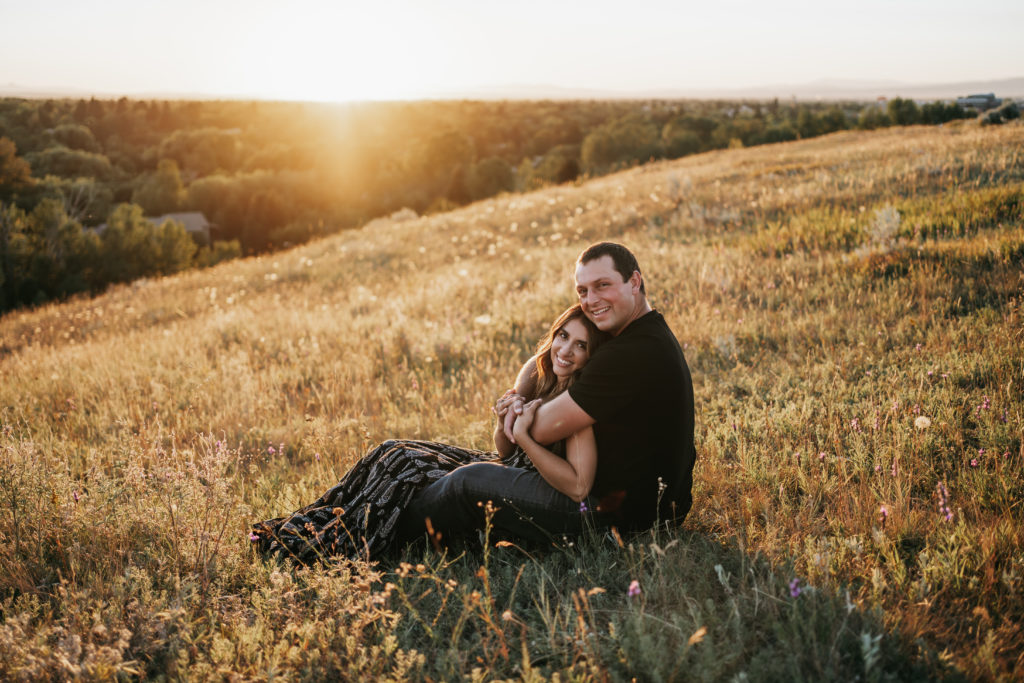 An engaged couple sitting in a field at sunset on a mountain in Bozeman, Montana.
