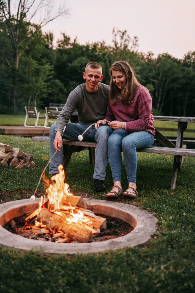An engaged couple roasts marshmallows by a campfire.