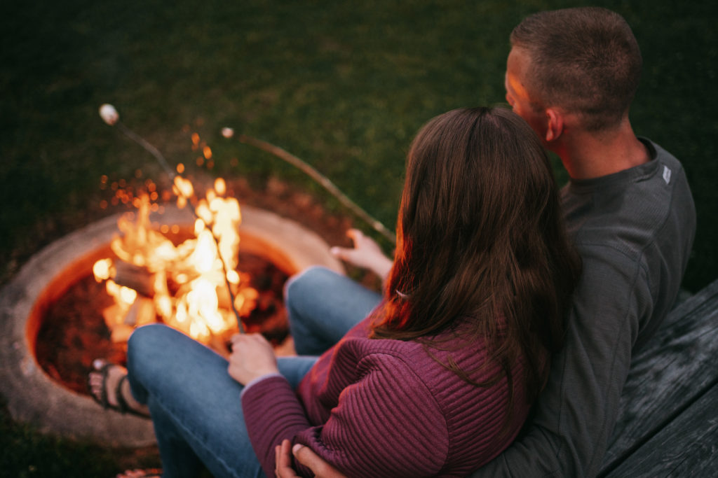 An engaged couple sits by a campfire.
