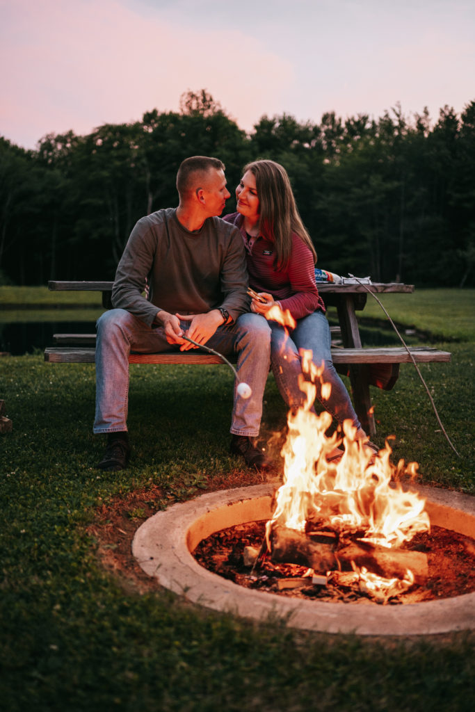 An engaged couple sits by a campfire.