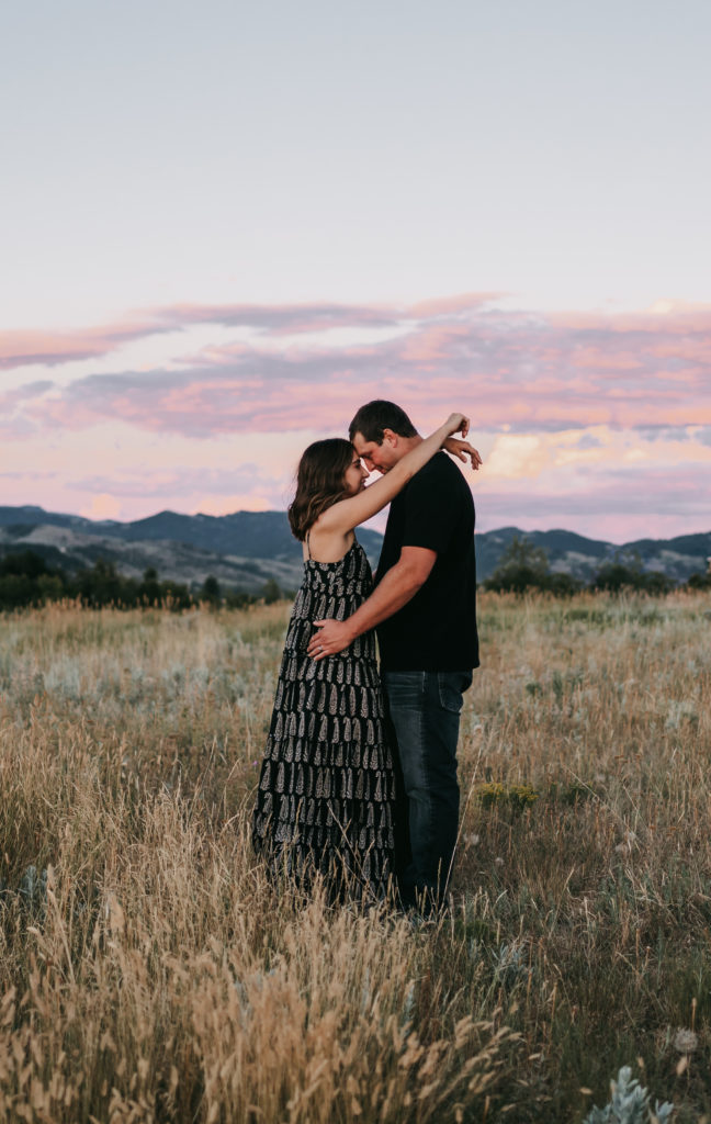 An engaged couple kissing during a purple and pink sunset on a mountain in Bozeman, Montana.