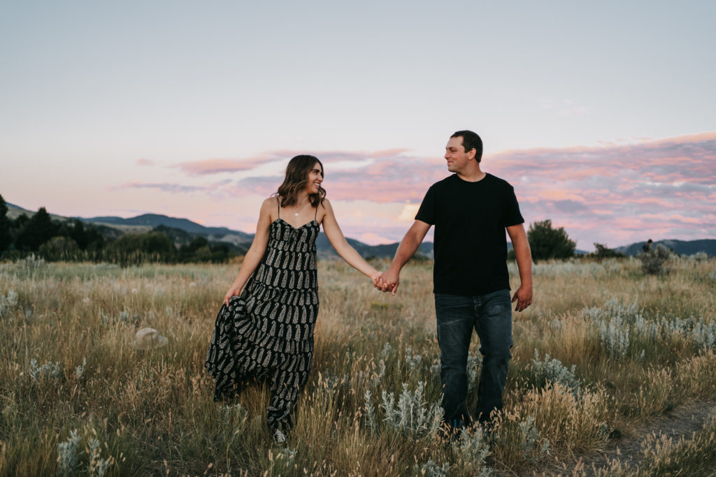 An engaged couple holding hands during a purple and pink sunset on a mountain in Bozeman, Montana.
