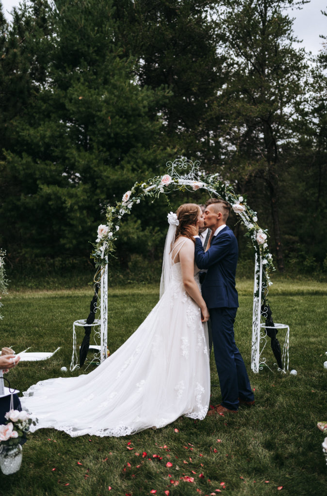 Bride and groom kiss under the arbor during their intimate wedding in Northern Minnesota
