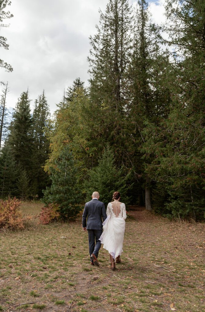 Newlyweds walk stroll hand-in-hand towards a grove of pine trees just off Ryan Beach in Glacier National Park.