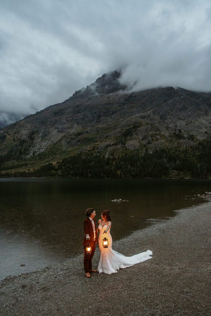 Newlyweds stroll along Pray Lake shoreline during blue hour, with camping lanterns in hand.