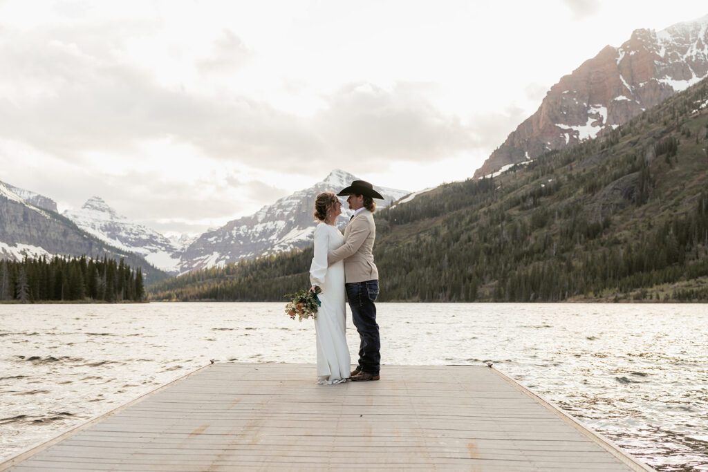 Bride and groom hug on a dock stretched over Pray Lake in Glacier National Park during their breathtaking mountain elopement.