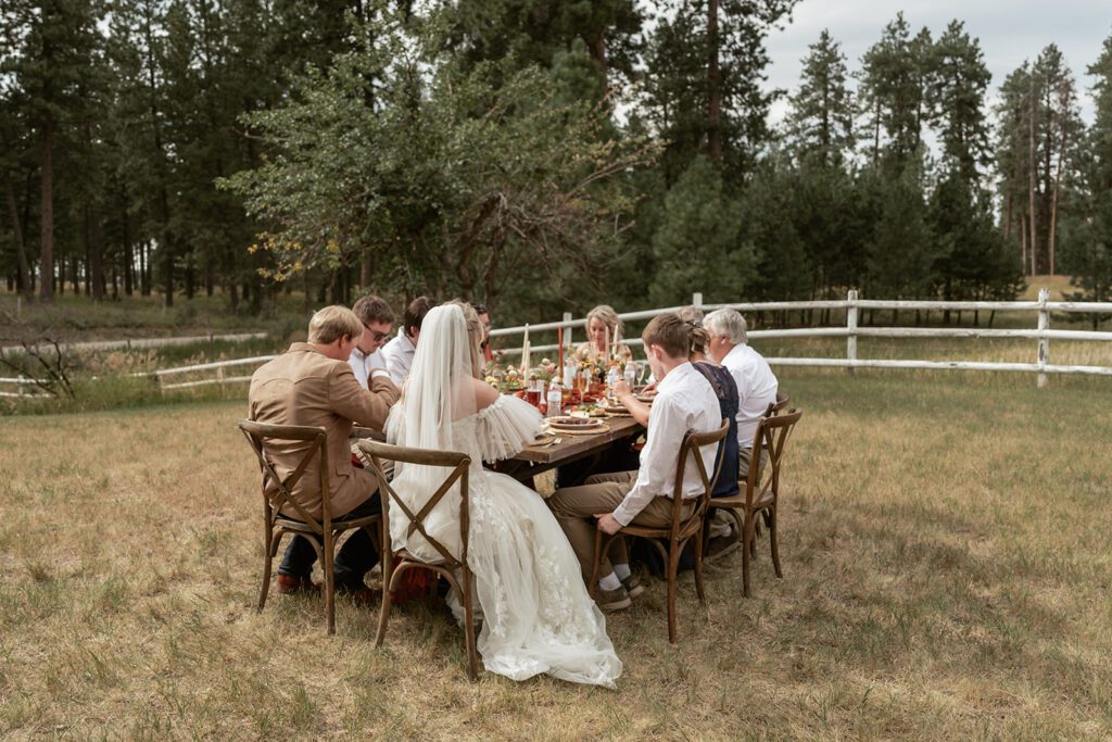 An intimate wedding dinner party beneath towering pines during a Northwest Montana microwedding photographed by Sydney Breann Photography