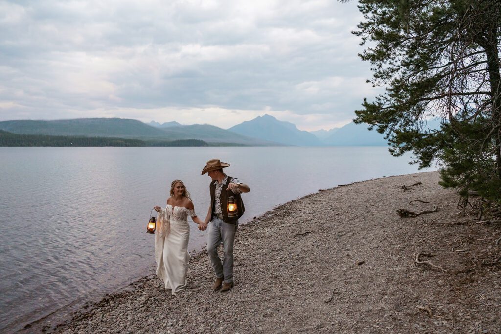 Bride and groom stroll hand-in-hand by the glow of lanterns at Lake McDonald during their care-free elopement in Glacier National Park