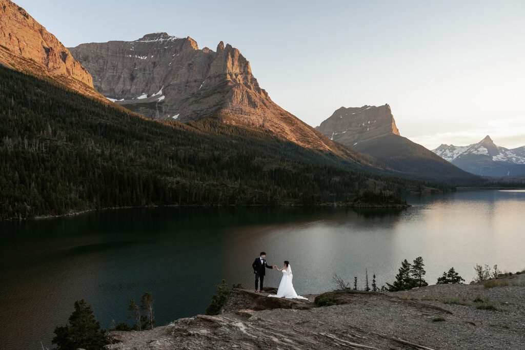 The sun begins to set at Sun Point as a classic bride and groom take in the stunning views during their whimsical evening adventure session in Glacier National Park