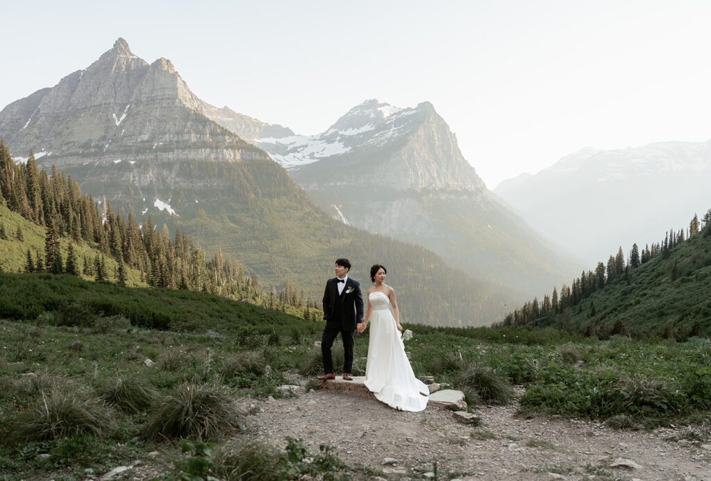 A classic bride and groom stroll through wildflowers at Big Bend in Glacier National Park during a whimsical evening adventure session