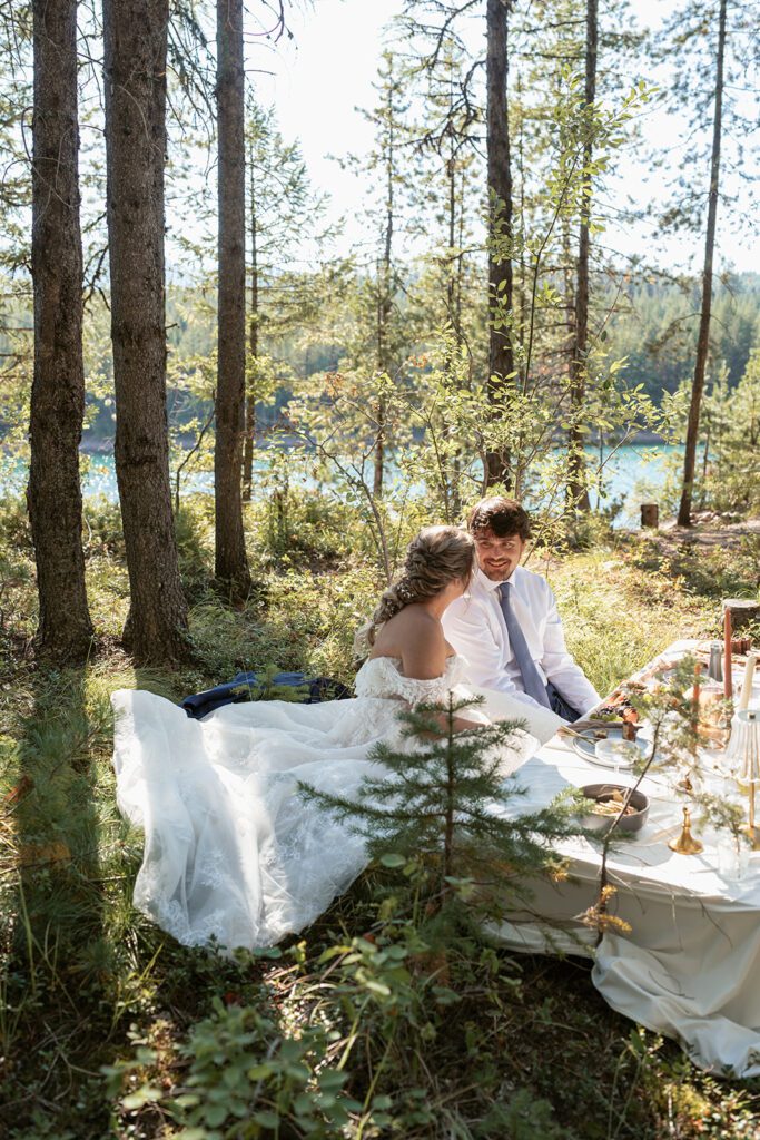 Newlyweds dine on a luxurious charcuterie picnic planned by Sydney Breann beneath towering pines overlooking Hungry Horse Dam.
