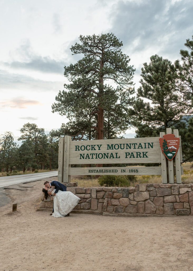 newlyweds kiss in front of the Rocky Mountain National Park welcome sign