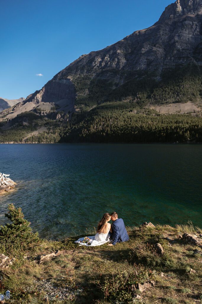 Newlyweds enjoy a picnic with an epic view overlooking blue waters in Glacier National Park