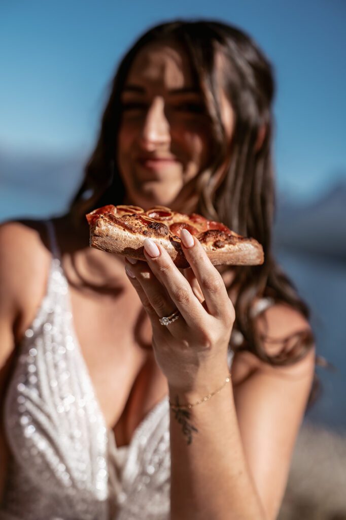 A bride enjoys pizza on the shore at Ryan Beach during an early Fall Elopement in Glacier National Park