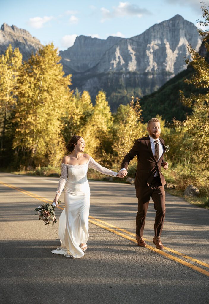 A couple frolics along a quiet road in Glacier National Park, among golden yellow aspen trees
